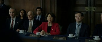 Movie still from “The Report” (2019), directed by Scott Z. Burns – A woman in a red jacket sitting at a table with three other people; Medium shot, Over the shoulder angle