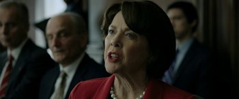 Movie still from “The Report” (2019), directed by Scott Z. Burns – An older woman wearing a red jacket and pearls; Close Up shot, Over the shoulder angle