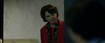 Movie still from “The Report” (2019), directed by Scott Z. Burns – An older woman wearing a red jacket and a floral scarf; Close Up shot, Over the shoulder angle