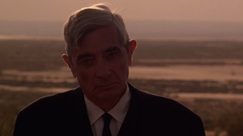 Movie still from “The Right Stuff” (1983), directed by Philip Kaufman – An older man wearing a suit and tie; Close Up shot, Over the shoulder angle