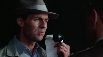 Movie still from “The Right Stuff” (1983), directed by Philip Kaufman – A man in a hat holding a microphone and a paper; Close Up shot, Low angle