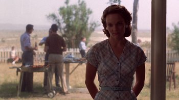 Movie still from “The Right Stuff” (1983), directed by Philip Kaufman – A woman standing in front of a grill with other people in the background; Medium shot, Over the shoulder angle
