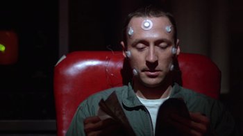 Movie still from “The Right Stuff” (1983), directed by Philip Kaufman – A man sitting in a red chair with a lot of magnets on his head; Close Up shot, High angle