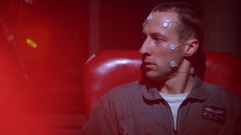 Movie still from “The Right Stuff” (1983), directed by Philip Kaufman – A man sitting in front of a red wall with white buttons on his head; Close Up shot, Low angle