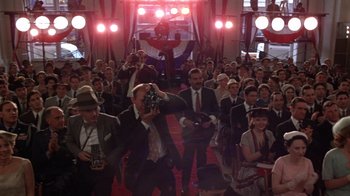 Movie still from “The Right Stuff” (1983), directed by Philip Kaufman – A group of people in suits and hats taking pictures; Wide shot, High angle