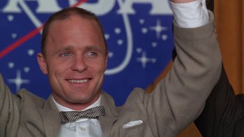 Movie still from “The Right Stuff” (1983), directed by Philip Kaufman – A man in a suit and bow tie raises his hand; Close Up shot, Low angle