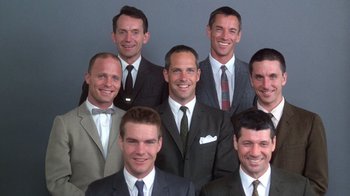 Movie still from “The Right Stuff” (1983), directed by Philip Kaufman – A group of men wearing suits and ties posing for a picture; Medium shot, Low angle