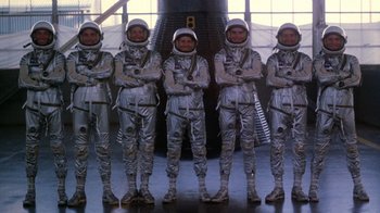 Movie still from “The Right Stuff” (1983), directed by Philip Kaufman – A group of men standing next to each other in space suits; Wide shot, Low angle