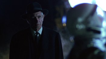 Movie still from “The Right Stuff” (1983), directed by Philip Kaufman – An older man in a suit and hat is standing in the dark; Close Up shot, Over the shoulder angle