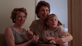 Movie still from “The Right Stuff” (1983), directed by Philip Kaufman – A woman and two women and a little girl sitting on a chair; Medium shot, Low angle