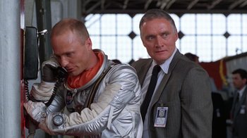 Movie still from “The Right Stuff” (1983), directed by Philip Kaufman – A man in a suit standing next to another man in a space suit; Medium shot, Low angle