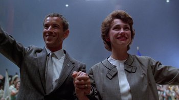 Movie still from “The Right Stuff” (1983), directed by Philip Kaufman – A man and a woman holding hands and smiling; Medium shot, Low angle