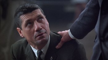 Movie still from “The Right Stuff” (1983), directed by Philip Kaufman – A man in a business suit being held by another man; Close Up shot, Over the shoulder angle