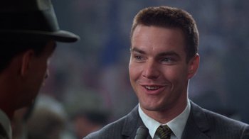 Movie still from “The Right Stuff” (1983), directed by Philip Kaufman – A man in a suit and tie smiling; Close Up shot, Over the shoulder angle