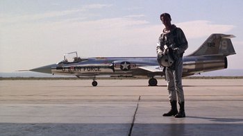 Movie still from “The Right Stuff” (1983), directed by Philip Kaufman – A man standing in front of an air force plane; Wide shot, Low angle