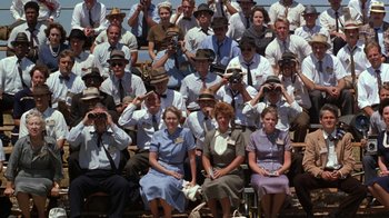 Movie still from “The Right Stuff” (1983), directed by Philip Kaufman – A group of people sitting on bleachers wearing hats; Wide shot, High angle