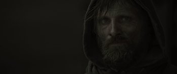 Movie still from “The Road” (2009), directed by John Hillcoat – A man with long hair and a beard wearing a hood; Close Up shot, Low angle