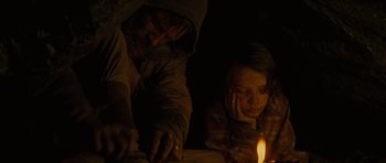 Movie still from “The Road” (2009), directed by John Hillcoat – A man and a woman are looking at a candle; Medium shot, High angle