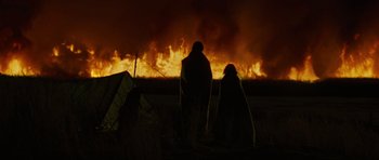 Movie still from “The Road” (2009), directed by John Hillcoat – Two people are standing in front of a burning field; Wide shot, Low angle
