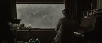 Movie still from “The Road” (2009), directed by John Hillcoat – A woman sitting in front of a window looking out at the sky; Wide shot, Over the shoulder angle