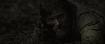Movie still from “The Road” (2009), directed by John Hillcoat – A man with long hair and a beard is holding a gun; Close Up shot, Over the shoulder angle
