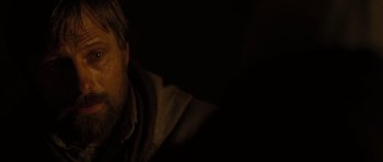 Movie still from “The Road” (2009), directed by John Hillcoat – A man sitting in a dark room with a dark background; Close Up shot, High angle