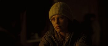 Movie still from “The Road” (2009), directed by John Hillcoat – A woman wearing a hat and a jacket looking at the camera; Close Up shot, Over the shoulder angle