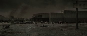 Movie still from “The Road” (2009), directed by John Hillcoat – An empty parking lot in front of an abandoned building; Extreme Wide shot, High angle