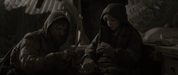 Movie still from “The Road” (2009), directed by John Hillcoat – Two people sitting under an open umbrella; Medium shot, Over the shoulder angle