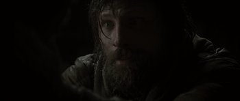 Movie still from “The Road” (2009), directed by John Hillcoat – A man with long hair and a goatee stares into the camera; Close Up shot, Over the shoulder angle