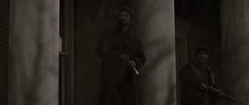 Movie still from “The Road” (2009), directed by John Hillcoat – A man holding a cigarette standing next to a brick wall; Medium shot, Low angle
