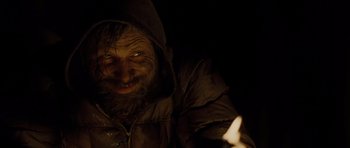 Movie still from “The Road” (2009), directed by John Hillcoat – A man with a beard is smiling at the camera while holding a lit candle; Close Up shot, Low angle