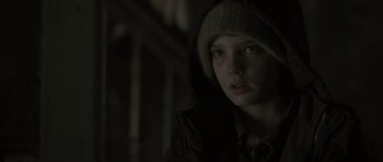 Movie still from “The Road” (2009), directed by John Hillcoat – A young girl wearing a hooded jacket in a dimly - lit room; Close Up shot, Over the shoulder angle