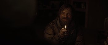 Movie still from “The Road” (2009), directed by John Hillcoat – A man holding a candle in a dimly - lit room; Medium shot, Over the shoulder angle