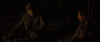 Movie still from “The Road” (2009), directed by John Hillcoat – An old man sitting in the woods at night; Medium shot, High angle