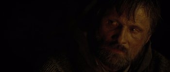 Movie still from “The Road” (2009), directed by John Hillcoat – A man with a long beard is looking at the camera; Close Up shot, Over the shoulder angle