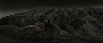 Movie still from “The Road” (2009), directed by John Hillcoat – A man walking with a baby carriage in the dark; Wide shot, High angle