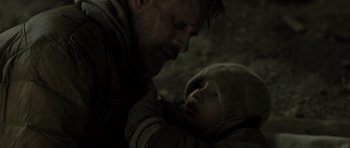 Movie still from “The Road” (2009), directed by John Hillcoat – A man holding a baby in his arms in the dark; Close Up shot, Over the shoulder angle