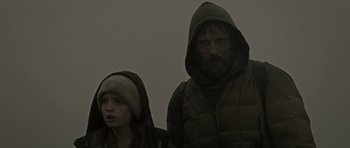 Movie still from “The Road” (2009), directed by John Hillcoat – A man and a woman wearing winter coats and hats; Medium shot, Low angle