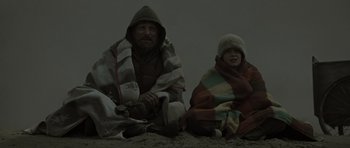 Movie still from “The Road” (2009), directed by John Hillcoat – A man and a child sitting on the beach wrapped in blankets; Medium shot, Low angle