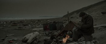 Movie still from “The Road” (2009), directed by John Hillcoat – A fire is burning on the ground in the desert; Wide shot, High angle