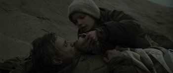 Movie still from “The Road” (2009), directed by John Hillcoat – A man and a woman in the sand with a cup; Close Up shot, High angle