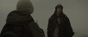 Movie still from “The Road” (2009), directed by John Hillcoat – A man with long hair wearing a jacket and hat; Medium shot, Over the shoulder angle