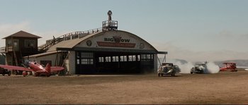 Movie still from “The Rocketeer” (1991), directed by Joe Johnston – An old truck parked in front of a building; Extreme Wide shot, Low angle