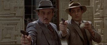 Movie still from “The Rocketeer” (1991), directed by Joe Johnston – A man in a suit and a man in a hat holding a gun; Medium shot, Low angle