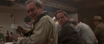 Movie still from “The Rocketeer” (1991), directed by Joe Johnston – Two men standing next to each other in a crowded room; Medium shot, Over the shoulder angle