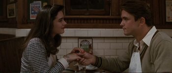 Movie still from “The Rocketeer” (1991), directed by Joe Johnston – A man and a woman sitting at a table holding hands; Medium shot, High angle