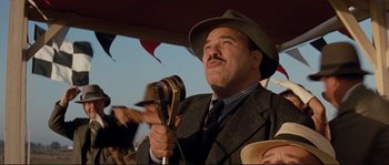 Movie still from “The Rocketeer” (1991), directed by Joe Johnston – A man in a suit and hat holding a microphone; Close Up shot, Low angle