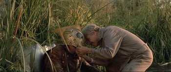 Movie still from “The Rocketeer” (1991), directed by Joe Johnston – An old man and a man with a mask in the grass; Medium shot, High angle