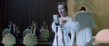 Movie still from “The Rocketeer” (1991), directed by Joe Johnston – A woman in a white dress is singing into a microphone; Medium shot, Low angle